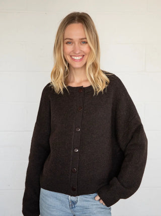 Woman wearing a dark brown cardigan over a black top with light blue jeans against a white background